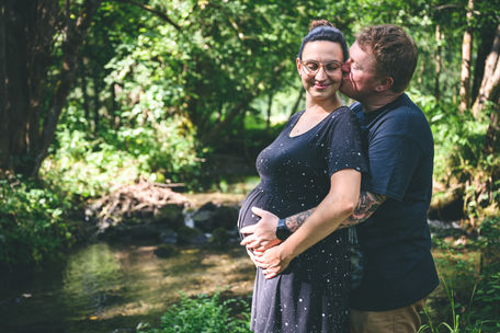 Vater umarmt die Mutter mit Babybauch und küsst sie auf die Wange