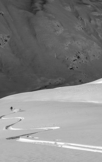 Ein Skifahrer fährt über unverspurten Pulverschnee mit einer Gruppe von mybergtour