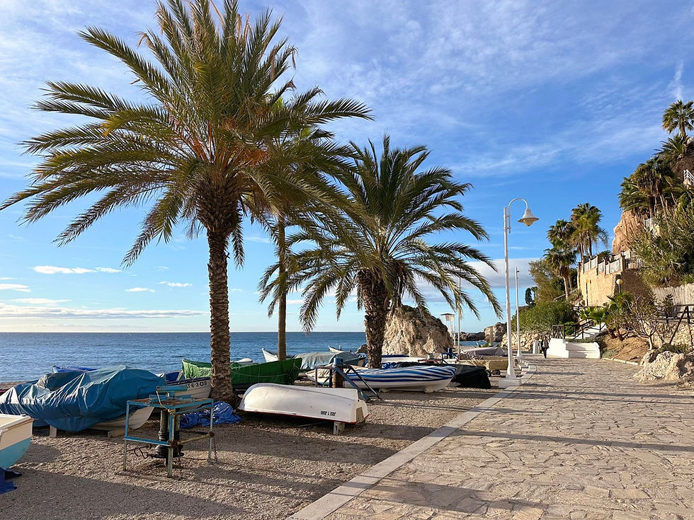 Aurinkoinen aamu Burriana -rannalla Nerjassa, kevyitä pilviä taivaalla, tyyni meri ja useita kalastusveneitä rannikon edustalla