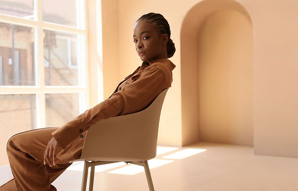 Black woman leaning black in chair near a window and staring at the camera