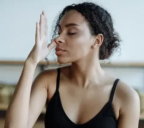 Woman practicing alternate nostril breathing during a yoga or meditation session, seated indoors and wearing a black tank top.