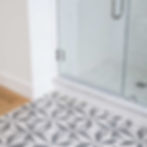 Geometric patterned tile floor next to a glass shower door in a modern bathroom.