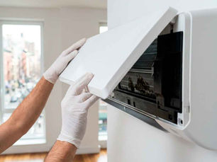 Professional cleaner in white nitrile gloves opening the front panel of a wall-mounted Daikin ductless mini-split AC unit to inspect for mold and biofilm in a bright New York City apartment