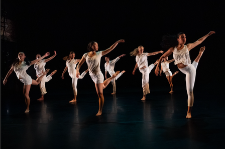 Dancers in white extending their legs in unison.