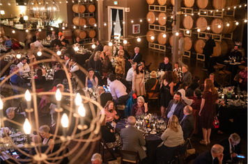Wide shot of a nonprofit gala at Domenico Winery in San Carlos, showing the stage and tables filled with seated guests.