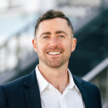 Executive headshot of a man in a dark blazer, dramatic urban background, San Francisco
