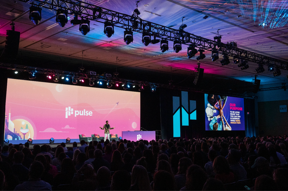 Keynote speaker on stage at a Conference at Moscone Center in San Francisco, with full audience and large branded screens, photographed by Nico Hend Photograph