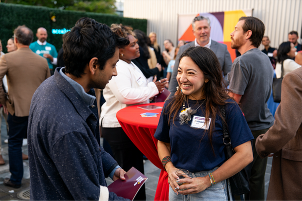 Two attendees smiling and talking beside a red cocktail table at the FFWD Demo Day reception.