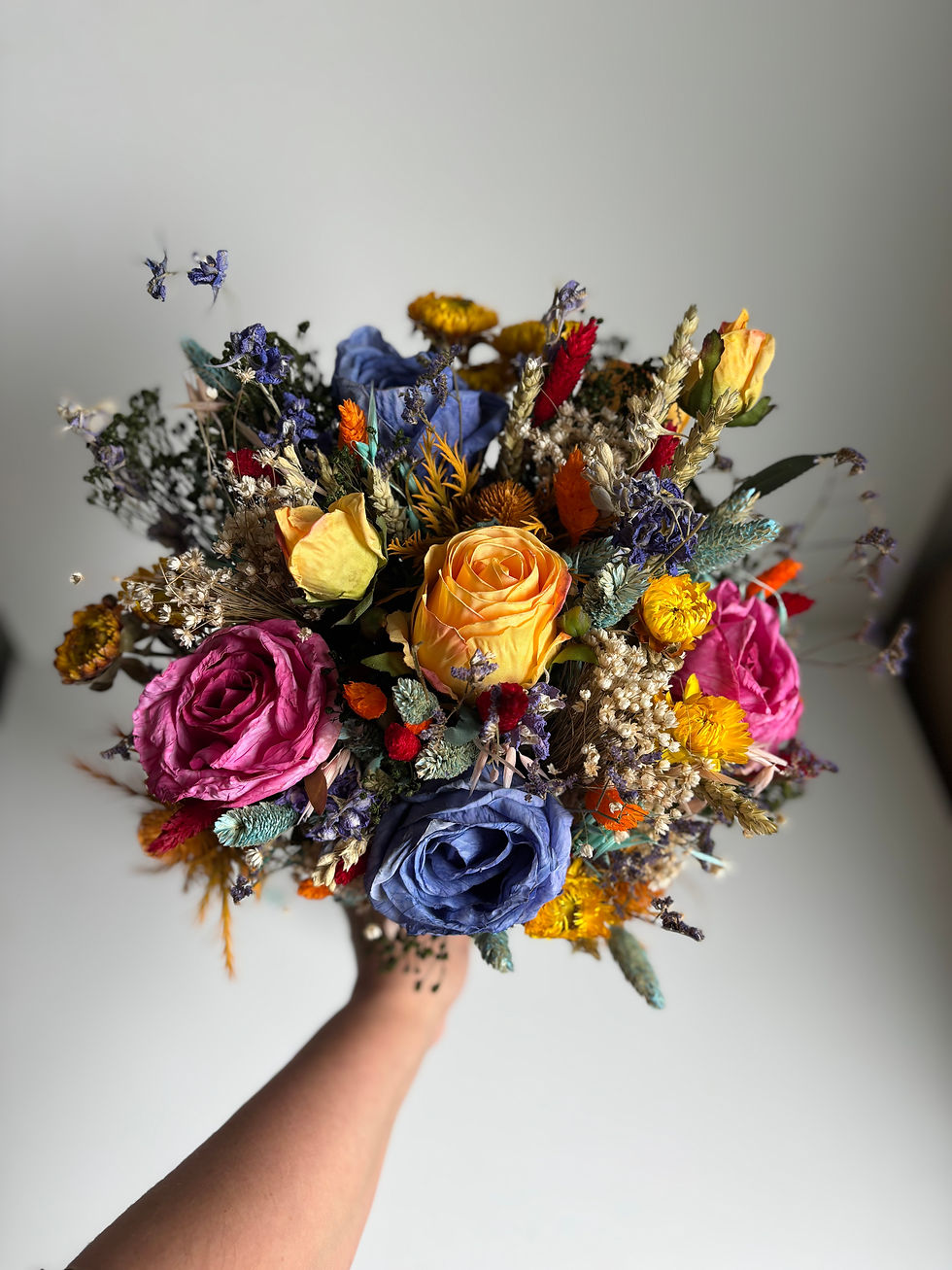 Thumbnail: Bright and colourful bridal bouquet with preserved pink roses, blue roses, yellow strawflowers and vibrant dried flowers.