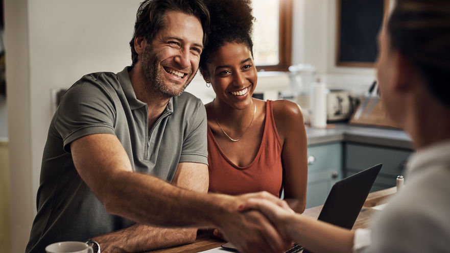 Investor and his wife shaking hands with an advisor while sitting a kitchen table.