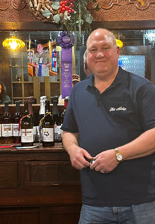 A photo of the owner, smiling and leaning against the counter at the wine bar.
