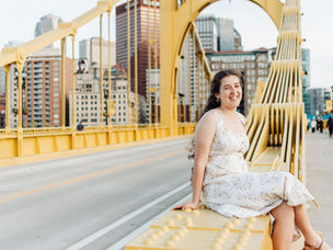 a girl in a floral dress poses on the Roberto Clemente bridge in downtown Pittsburgh for her senior photo session