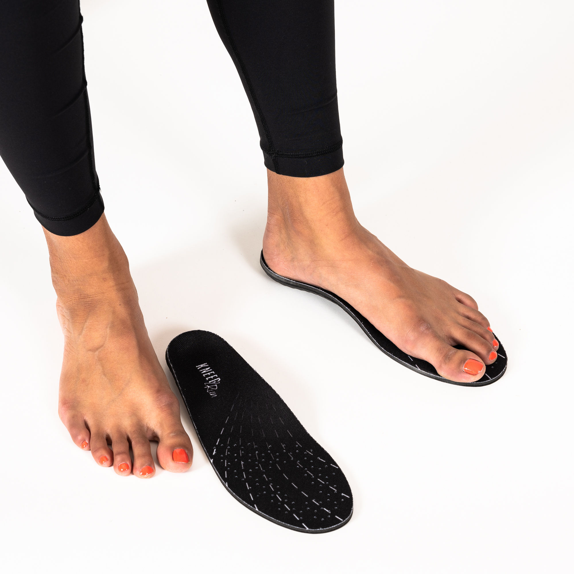 A pair of feet near a pair of off-the-shelf Kneed insoles in the Kneed2Run version that provide arch support in athletic shoe