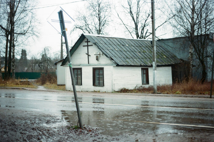 Analog photography picture of a white house orthodox church next to a rainy street in winter on Russian countryside in Leningrad oblast Russia