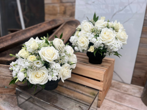 Two white rose floral arrangements on wooden crates.