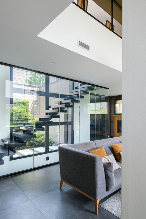 Salon contemporain de luxe avec verrière, mobilier design, plafond haut et éclairage suspendu, dans une villa moderne conçue par un architecte à Lyon, France, escalier métal devant patio