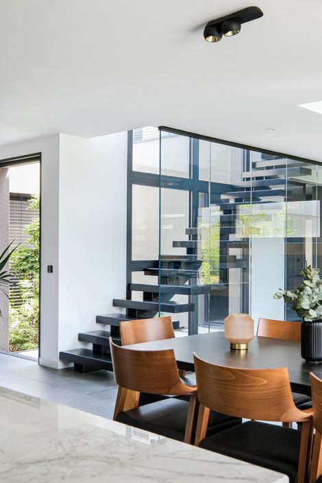 Salon contemporain de luxe avec verrière, mobilier design, plafond haut et éclairage suspendu, dans une villa moderne conçue par un architecte à Lyon, France, escalier métal devant patio