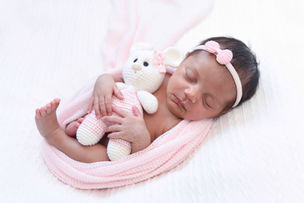 Bebê recém-nascida envolvida em wrap decorado segurando ursinho de crochê durante ensaio newborn.