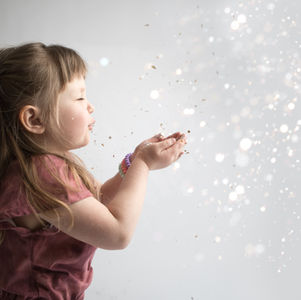 a little girl blows glitter into the air