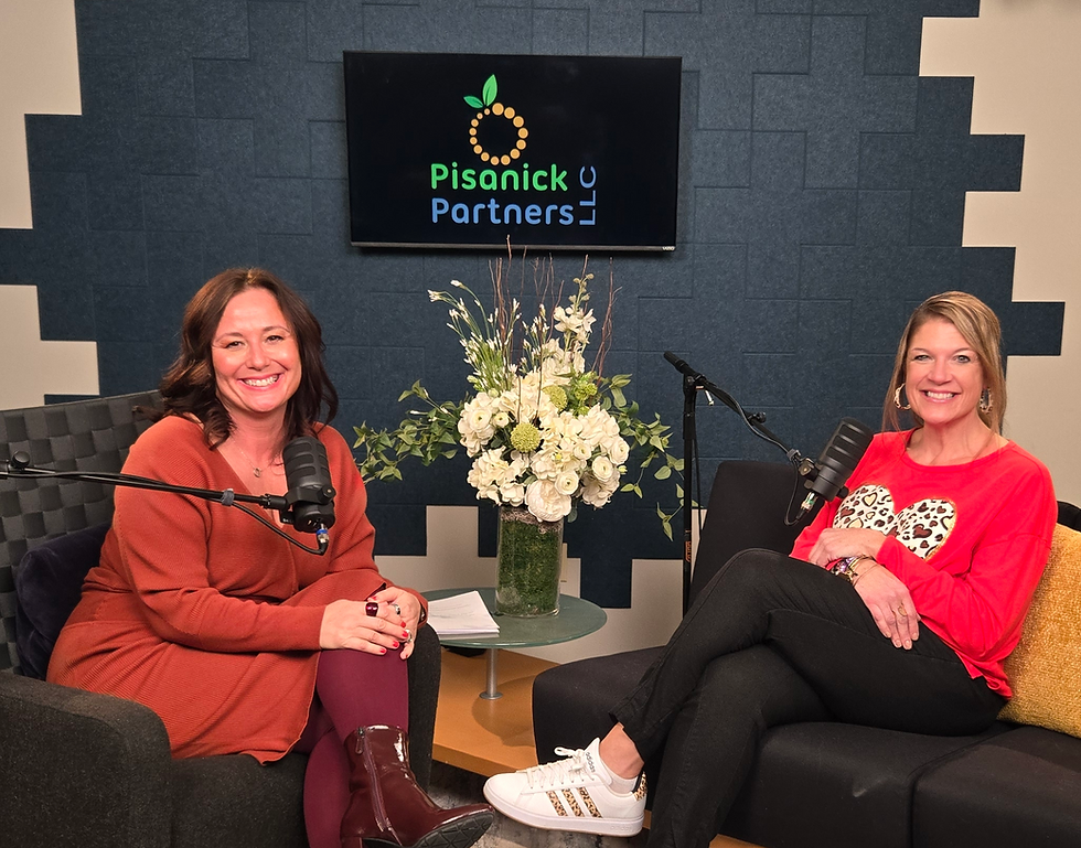 Two smiling women sit with microphones in a podcast studio; Pisanick Partners LLC logo on screen behind white flowers.