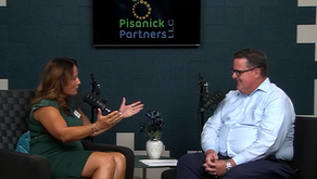 Woman in green interviews smiling man in podcast studio; Pisanick Partners LLC logo on screen above microphones.