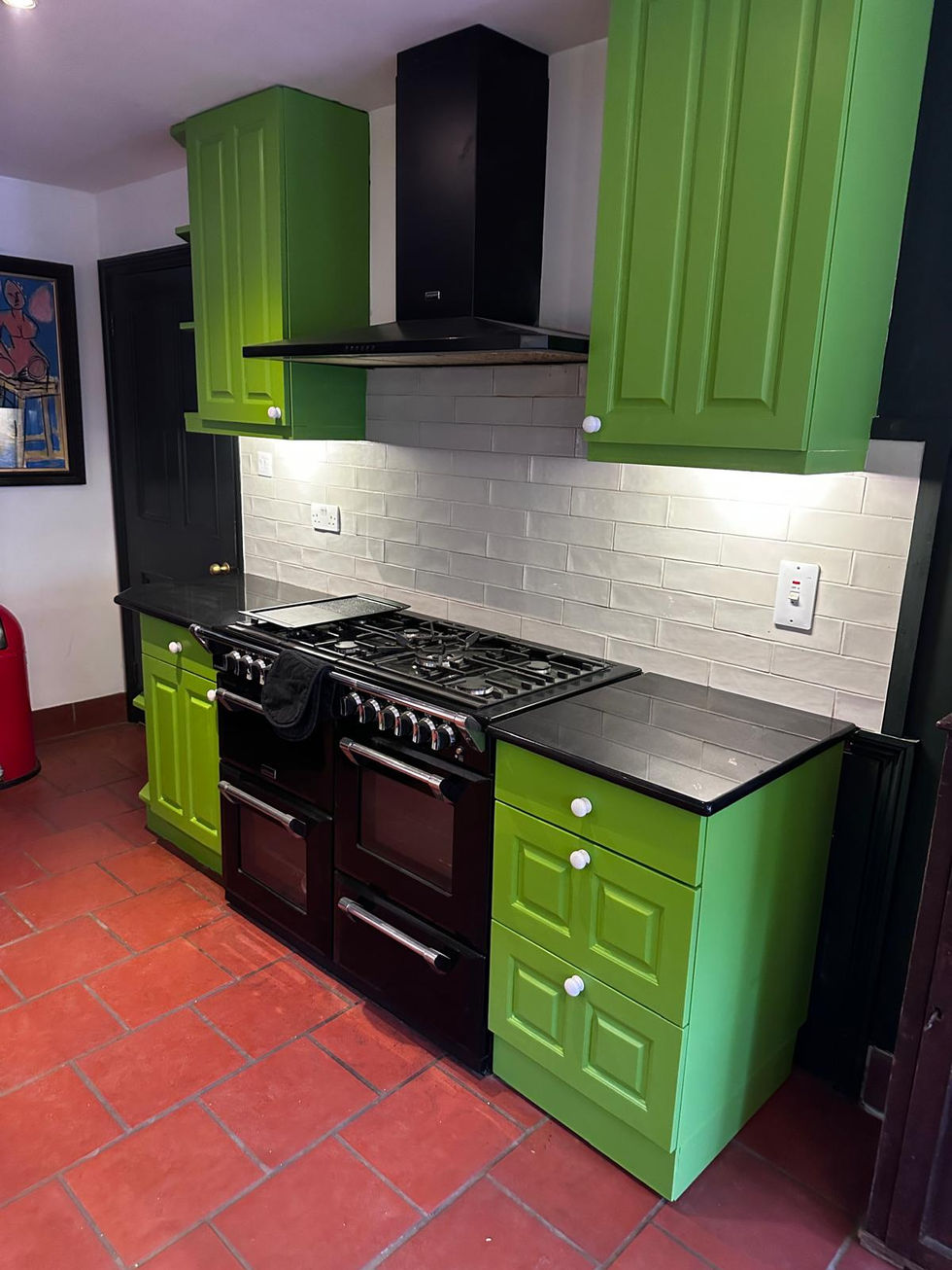 Green painted kitchen cabinets with black range cooker and white tiled splashback
