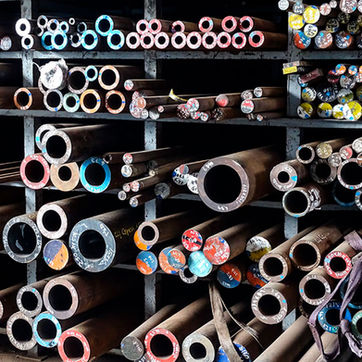 Barras de acero redondas y tubulares almacenadas en estanterías industriales, con los extremos pintados de diferentes colores para identificar el tipo de aleación y grado de acero.