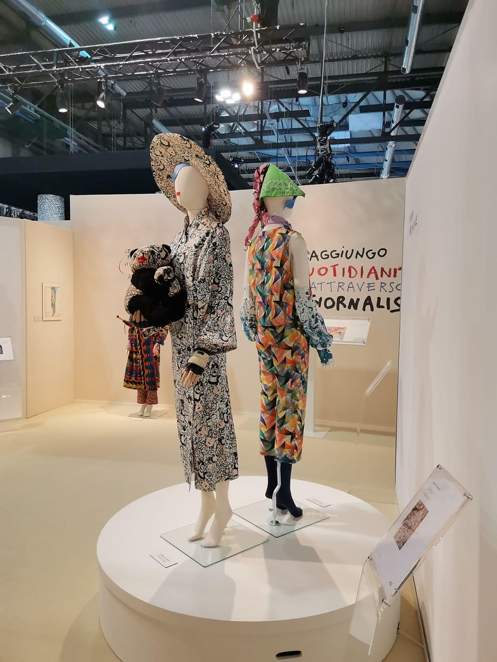 Mannequins display a variety of designer outfits with striking patterns and large accessories in a contemporary exhibition setting. © MBA Photography