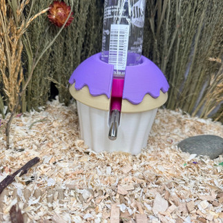 A hamster water bottle stood in a purple, cream and white coloured cupcake shaped 3D printed water bottle holder