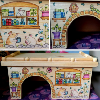 Wooden hamster hide decorated with books, an owl, 2 hamsters under a window and a little mouse in the window