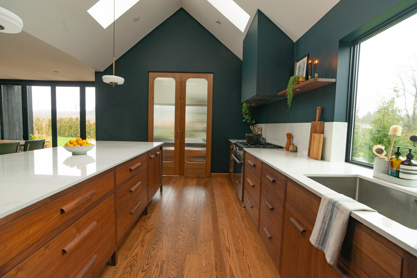 Fully custom walnut kitchen with integrated cabinetry, large island with stone countertop, and floor-to-ceiling pantry storage in a modern, light-filled space.