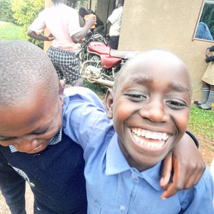 Two 10-year old girls laugh and smile, hugging and holding onto each other. They wear blue school uniforms. 