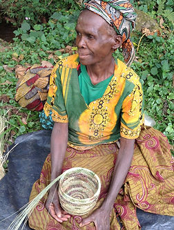 Frida a Batwa elder female holds a basket she is in the process of weaving