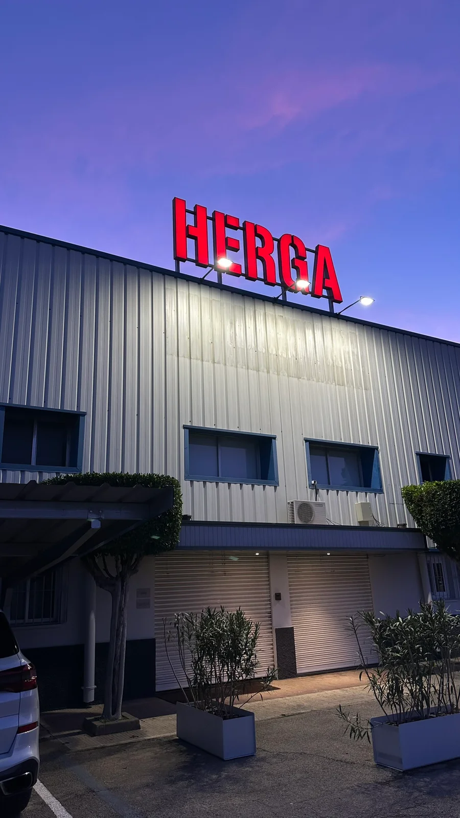 Fachada de la nave de Herga con el rótulo iluminado al anochecer