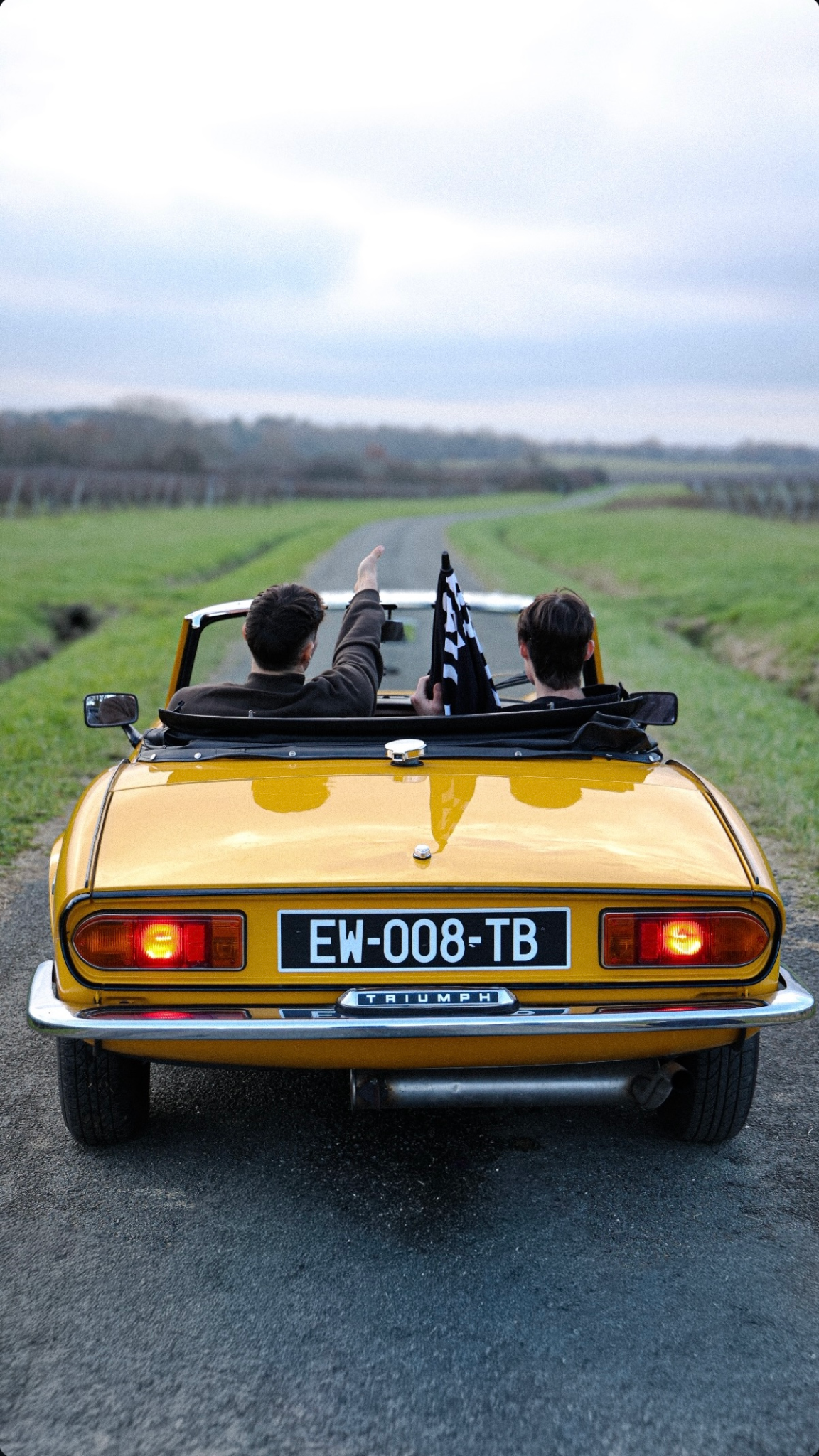 Triumph Spitfire jaune sur une route de vignobles