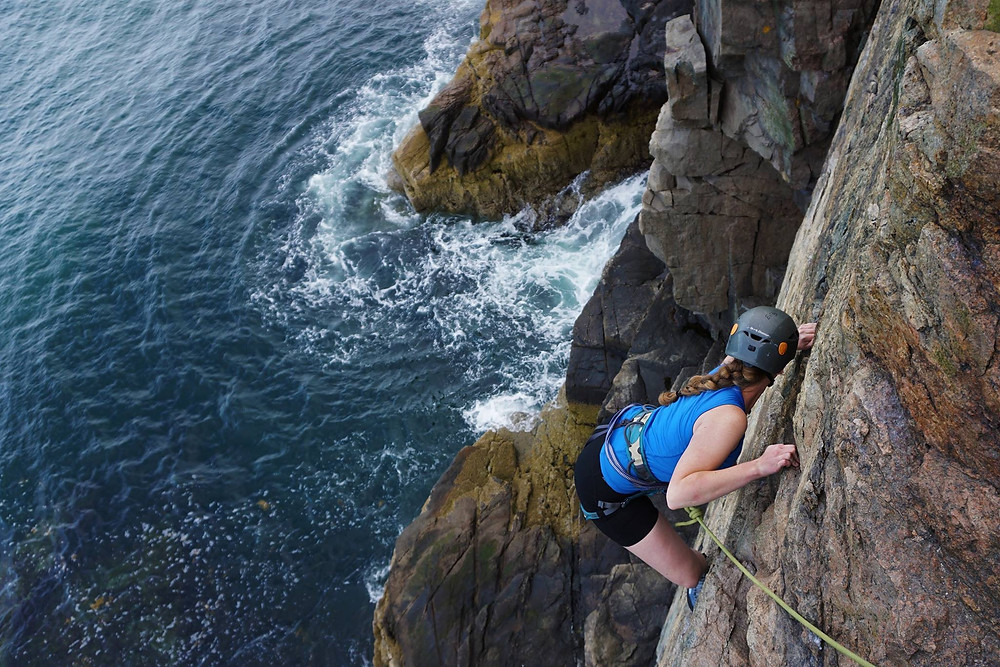 a female solo traveler takes a photo while climbing a cliff over the ocean