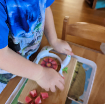 A child is using a kitchen tool to cut fruit. 