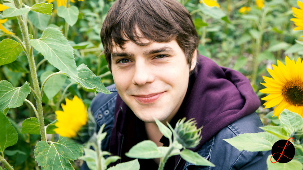 Junger Mann hockt im Sonnenblumenfeld und lächelt. 