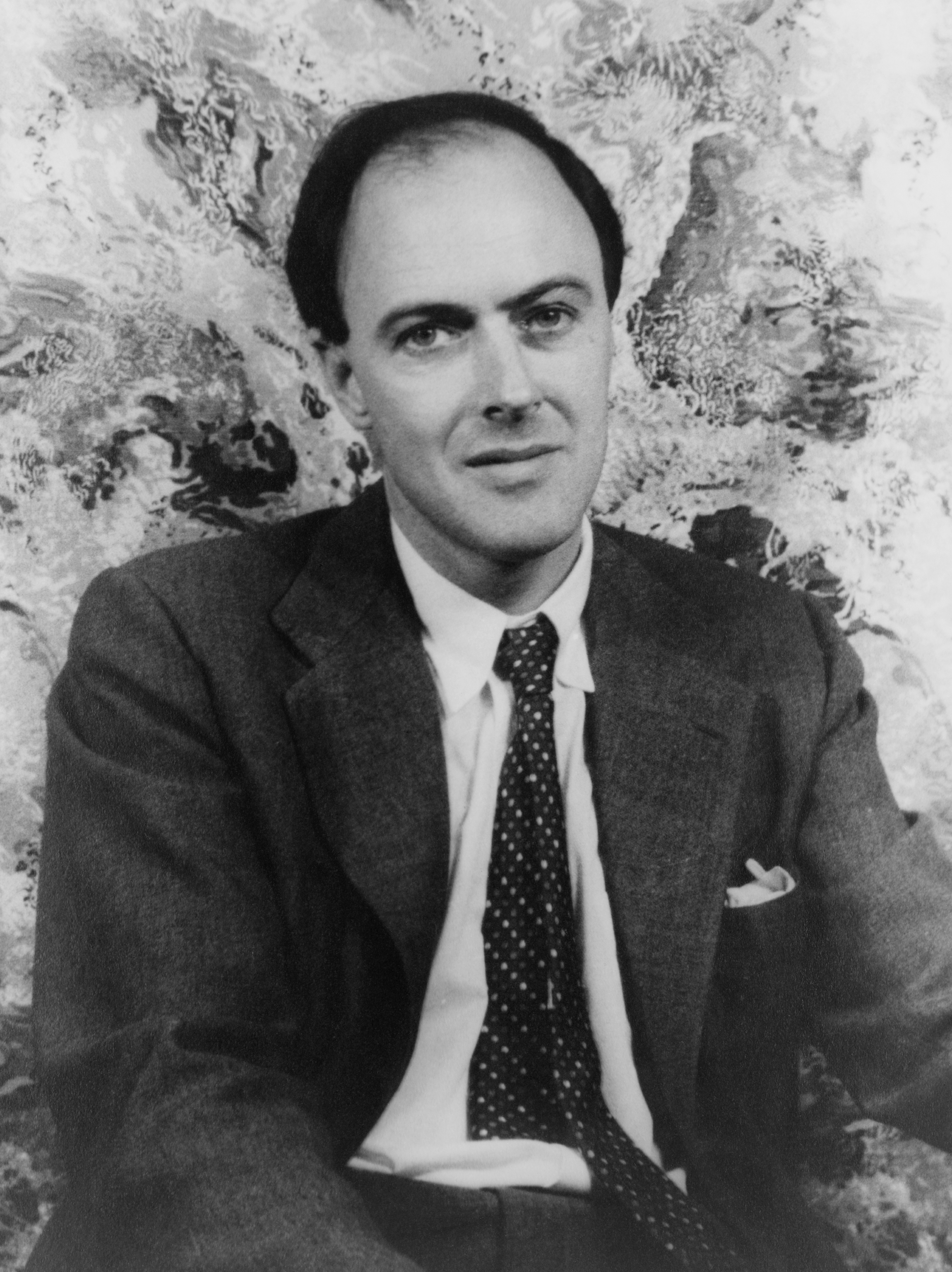 A black-and-white portrait of author Roald Dahl seated indoors.