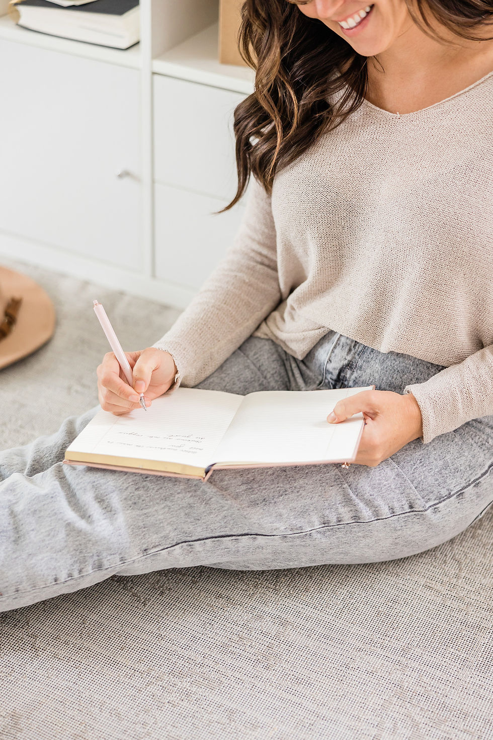 Smiling woman writing in a notebook while sitting on floor.