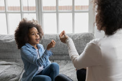 Close up African American mother teaching disabled daughter, showing symbols, little girl 