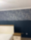 A feature bedroom wall with dark blue panelling below and a blue and white patterned wallpaper above