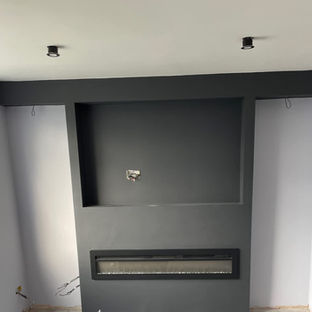 A room under renovation featuring a modern, dark grey media wall with an integrated electric fire