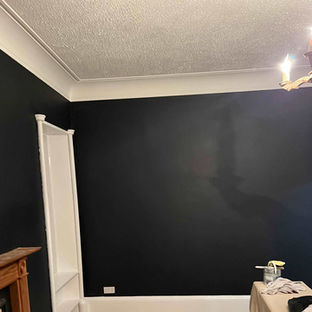 A living room with one dark blue feature wall, a wooden floor, and paint cans ready for decorating