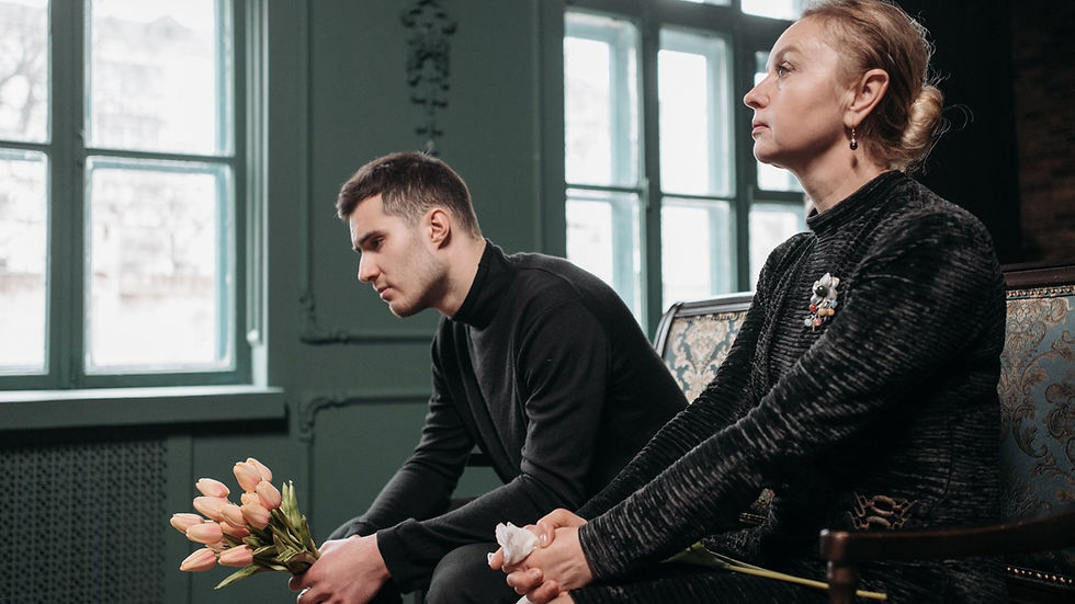Two individuals in mourning attire sitting solemnly indoors, reflecting sorrow.
