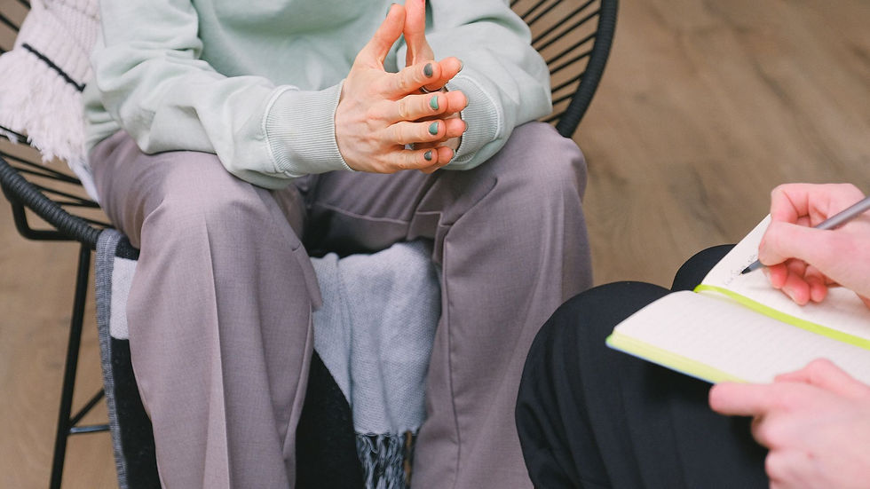 Crop unrecognizable psychotherapist taking notes in journal while interacting with woman on chair during psychological counseling indoors
