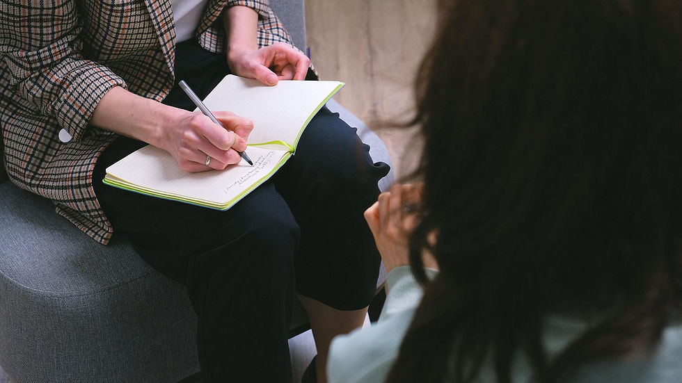 From above of crop anonymous psychotherapist taking notes in agenda while speaking with woman during psychological session