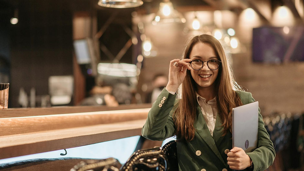 Confident businesswoman in green blazer holding laptop at a chic bar with warm lighting.