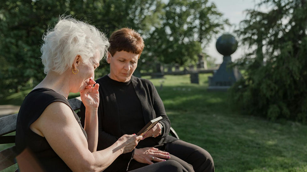 Two women sitting on a bench in a cemetery, sharing a moment of remembrance.