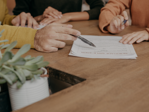 Hands hold pens, reviewing a mortgage application on a wooden table. A potted plant is in the foreground, creating a focused atmosphere. Canadian mortgage rates remain high in 2025 – buyer frustration and lender strategy concept